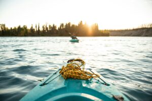 View from the bow of a kayak on a calm lake at sunset with another kayaker in the distance
